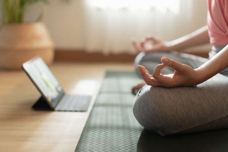 Close up of hand woman doing lotus yoga exercises on yoga mat with Training online on the tablet at home morning, Concept of relaxation and meditationの写真素材