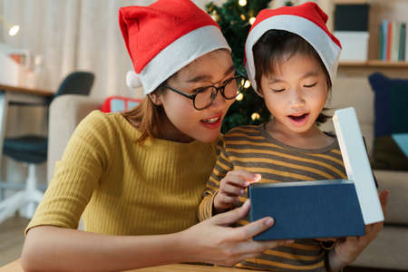 Happy Asian family with mother and daughter open Christmas present gift box together on holiday at homeの写真素材