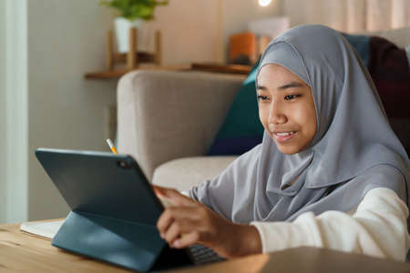 Muslim girl doing homework and using tablet with tutor via the internet on a table at night.の写真素材