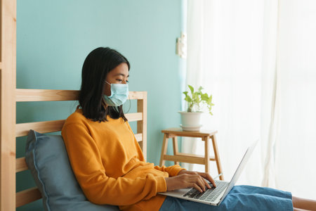 Asian woman wear medical mask while sitting  learning online with laptop computer at home, Concept online learning at homeの写真素材