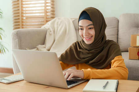 Muslim young women wear hijab using typing and checking order the customer address on the computer laptop at home morning. Concept business small and shop onlineの写真素材