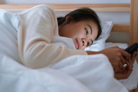 Asian woman using a smartphone while lying in the bedroom at the nightの写真素材
