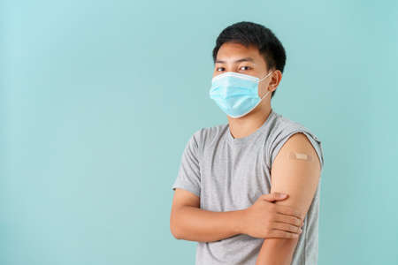 Asian men wearing face mask vaccinated Showing arm bandage to protect  spread on blue background.の写真素材