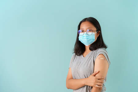 Asian women wearing face mask vaccinated Showing arm bandage to protect spread on blue background.の写真素材