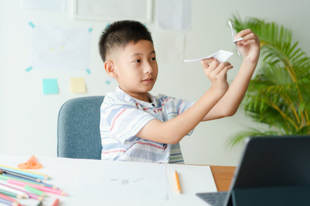 asian boy playing paper airplane while sitting at home morning, asia men  learning online with teacher on tabletの写真素材
