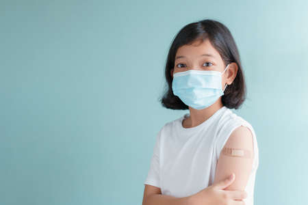 Asian little girl wearing facemask vaccinated Showing arm bandage to protect spread on blue backgroundの写真素材