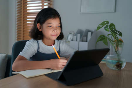 Asian little girl do homework and learning online via the internet tutor on tablet digital night, Concept of online learning at homeの写真素材