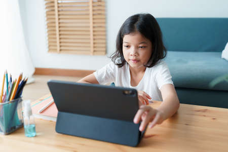Asian little girl learning online via the internet tutor on a tablet while sitting in the living room at morning, Concept of online learning at homeの写真素材