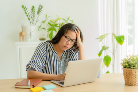 Asian woman suffering stress working on laptop in overwork. Tired businesswomen using a computer.  She use her hand to touch her face, Asia girl feeling sadの写真素材