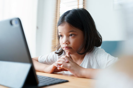 Boring asian girl is studying online via the internet on tablet while in the living room at home morning, Asian elementary school children watching computer tablet. Concept distance learning at homeの写真素材