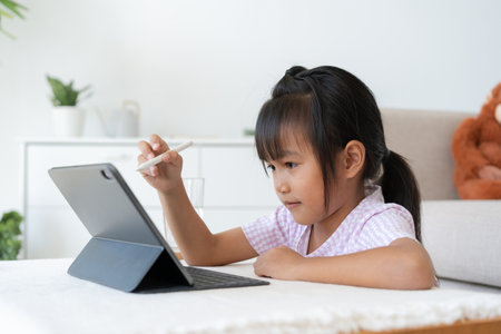 Education. Asian little girl learning and drawing with the online teacher on tablet digital, Application on mobile at home morning, Side viewの写真素材