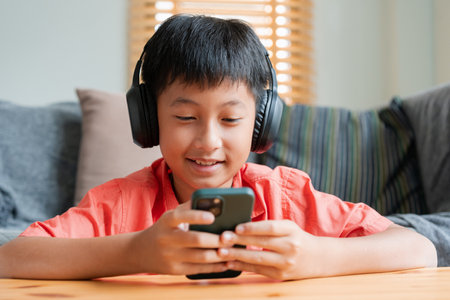 Portrait. Asian boy playing online game on smart phone with headphones . Asia man using mobile phone happy smile at home the morning sunlightの写真素材