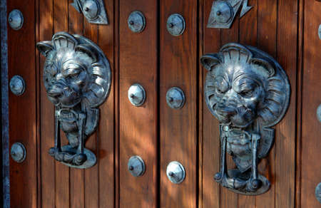 very large lion's head door knocker on wooden door surrounded by large rivets and large hinges.の写真素材