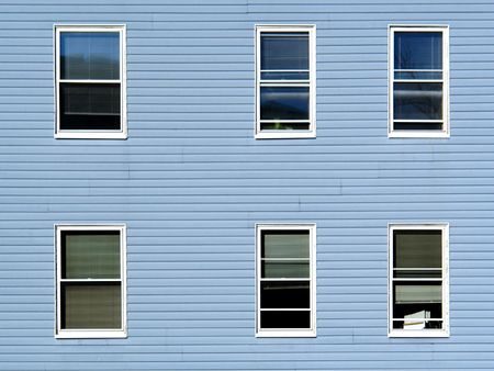 six windows on an apartment building in the sunshine, the building is covered in blue vinyl siding