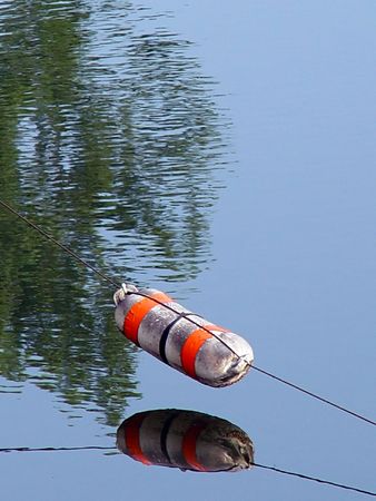 orange and white buoy suspended over water with trees reflecting in the pondの写真素材