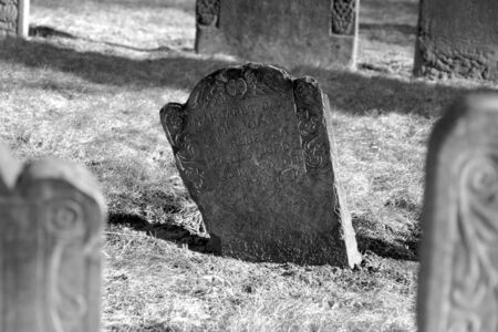 a dark stone stands out in this scene of ancient grave stones in black and white in bright sun light on a beautiful winter's dayの写真素材