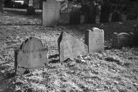dramatically lit ancient grave stones in black and white in bright sun light on a beautiful winter's dayの写真素材