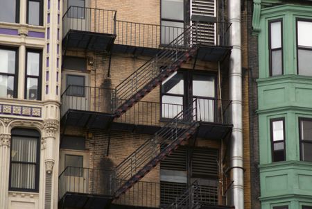 three buildings and a fire escape, plain brick, one colorfully painted  and the other a simple paint...