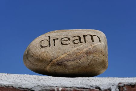 dreams put on the shelf, a rock with the word dream inscribed in it  sits on top of a brick wall against a deep blue skyの写真素材