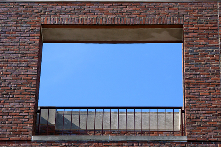 blue sky is framed by a large opening in a brick wall with railing on balconyの写真素材