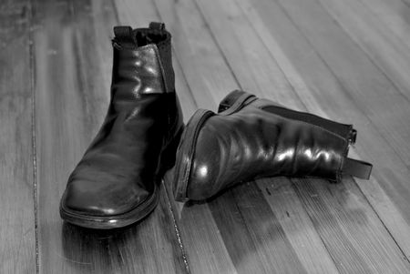pair of old black leather boots in the sunshine on a dirty pine wood floor