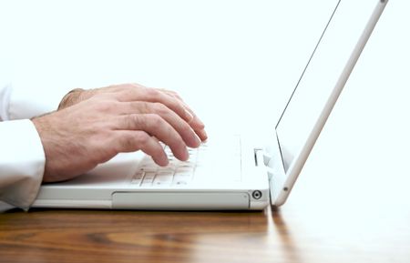 man sitting at desk typing on the keyboard of a white laptopの写真素材