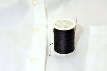 spool of black thread on white shirt with needle
