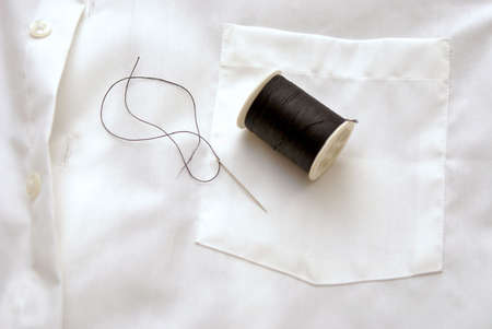 spool of black thread on white shirt with needle, laying on pocketの写真素材