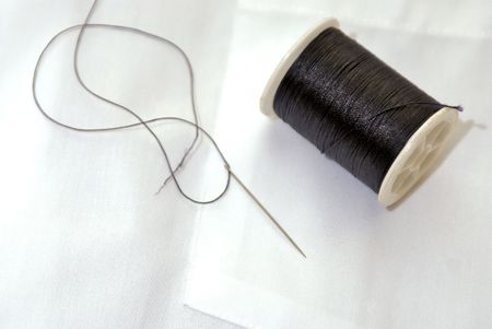 spool of black thread on white shirt with needle, needle is threadedの写真素材
