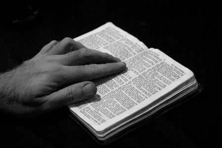 hand of man resting on bible, reading the book of saint matthew, on black background