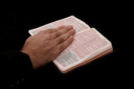 hand of man resting on bible, reading the book of saint matthew, on black background