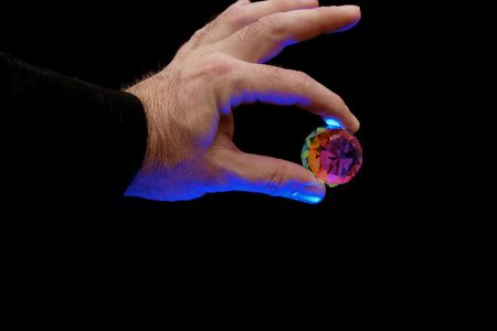 magician holding faceted crystal, theatrical blue lighting illuminates the hand against a black...