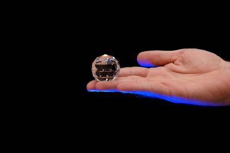multi faceted crystal globe sitting on finger tips of a man lit from below with blue theatrical lighting against a black backgroundの写真素材