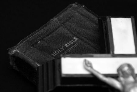 striking black and white image of an old crucifix laying on top of an ancient leatherbound bibleの写真素材