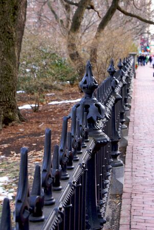ornate wrought iron fence running along brick sidewalk on a winter dayの写真素材
