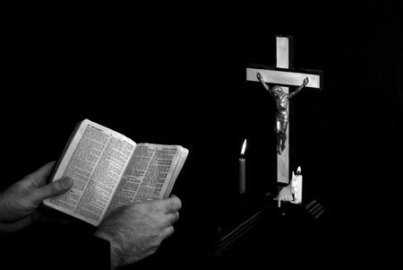 man reading bible near prayer crucifix with candles burning, book is open to st. matthew
