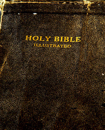 detail of the cover of an old antique holy bible with gold text stamped into the richly textured cover that is tattered and well wornの写真素材