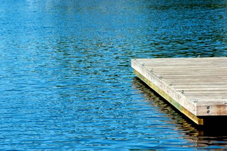 wooden pier with metal eye hooks surrounded by deep blue water with ripplesの写真素材