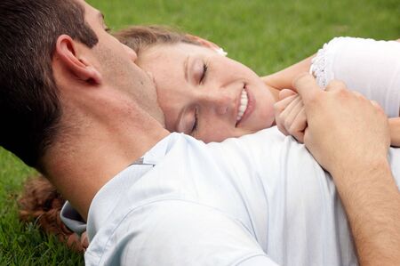 smiling woman with eyes closed resting her head on her lover's chest as he kisses her forehead as...