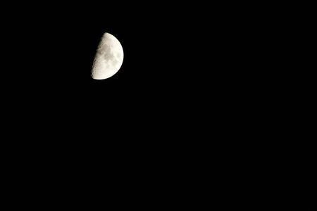 A half full waxing moon is located in the upper left of the image against a drak sky providing...