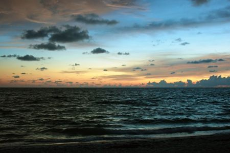 a pastel sunset creates the backdrop for the waves rolling into the shore at the beach.の写真素材