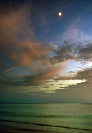 swirling clouds fill the sky as the moon shines bright at sunset over the seaの写真素材