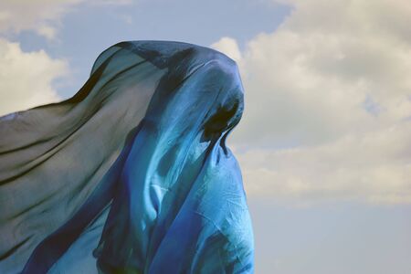 a blue silk cloth forming abstract shape against a cloud filled skyの写真素材