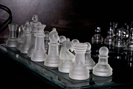 shown at an angle, a frosted glass chess set on a glass chess board with a dark background, opponents pawns can be seen in the backgroundの写真素材