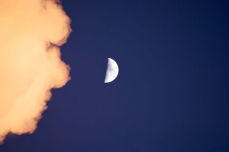 a cloud moves in towards the moon as the sunsets in early eveningの写真素材