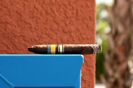 a large cuabn cigar is laying on blue container with red wall in background with palm treeの写真素材