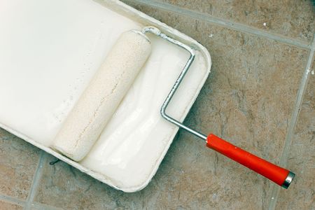 a used paint roller is sitting in pan with paint on floor.の写真素材