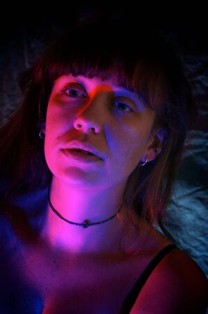 a beautiful yooung woman looking slightly to the side in a dark room lit with red and blue lights