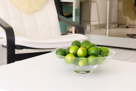 A bowl of fresh limes is placed on a white table inside a home.の写真素材