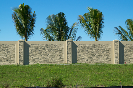 A wall stretched across the image, on top of a hill with palm trees on the other side of the wall against a blue sky on a sunny day.の写真素材